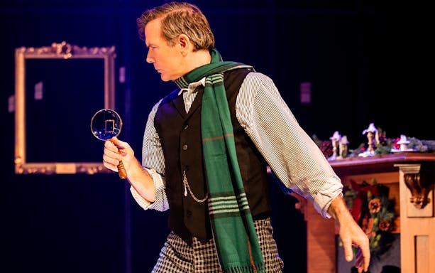 Detective with magnifying glass in "A Sherlock Carol" stage scene.