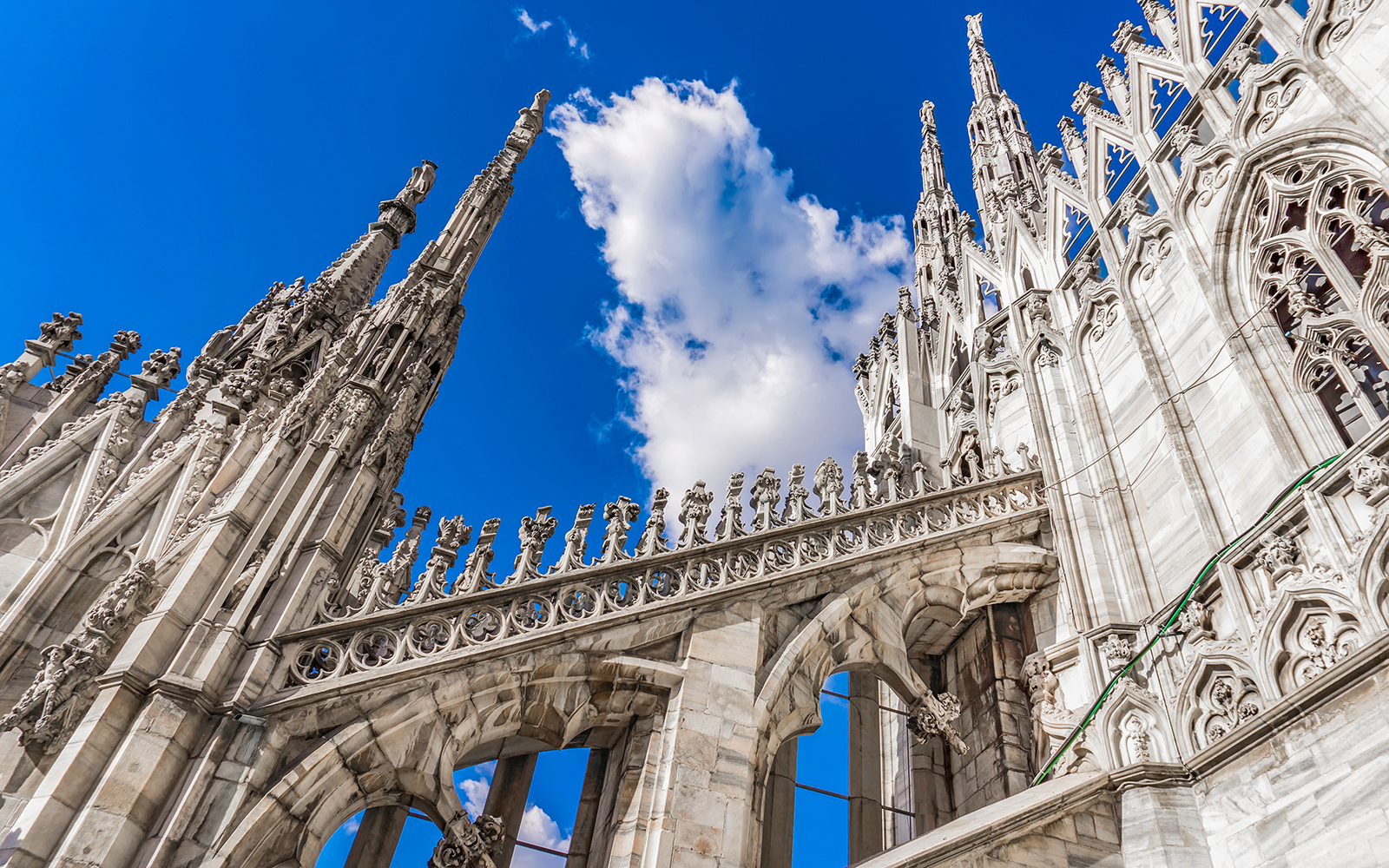 Duomo Cathedral rooftop spires and ornate architecture against blue sky, Milan, Italy.