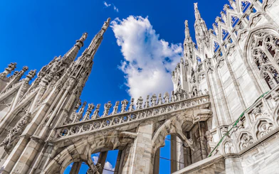 Duomo Cathedral rooftop spires and ornate architecture against blue sky, Milan, Italy.
