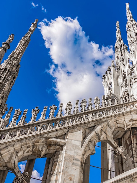 Duomo Cathedral rooftop spires and ornate architecture against blue sky, Milan, Italy.