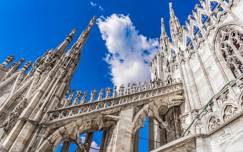 Duomo Cathedral rooftop spires and ornate architecture against blue sky, Milan, Italy.
