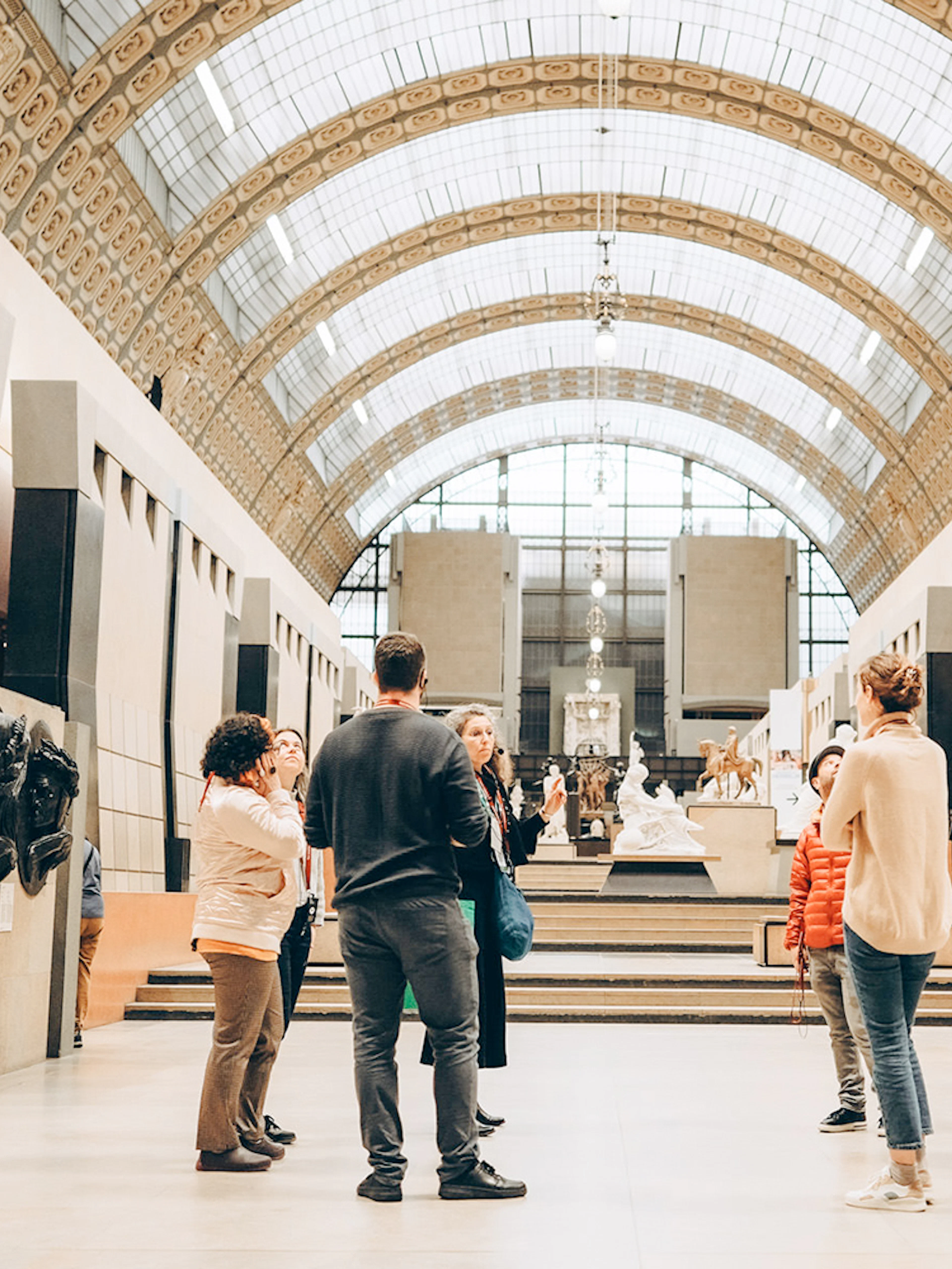 Tour guide with group inside Orsay Museum, Paris, near sculptures and art displays.