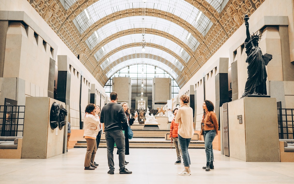Tour guide with group inside Orsay Museum, Paris, near sculptures and art displays.
