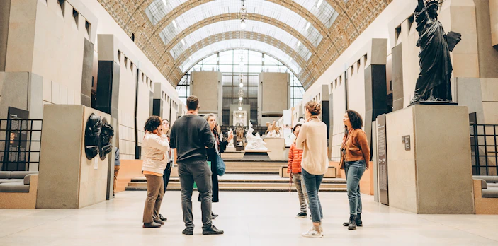 Tour guide with group inside Orsay Museum, Paris, near sculptures and art displays.