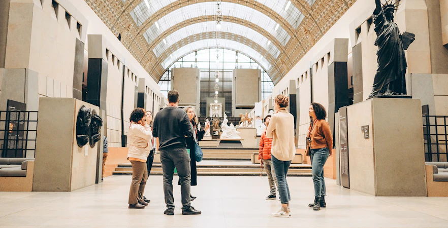 Tour guide with group inside Orsay Museum, Paris, near sculptures and art displays.