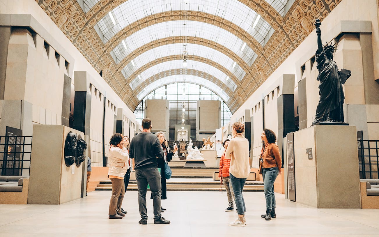 Tour guide with group inside Orsay Museum, Paris, near sculptures and art displays.