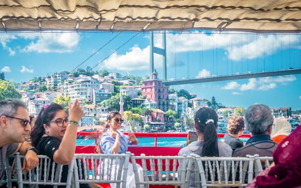 Guests on Bosphorus cruise with view of bridge and Istanbul skyline.