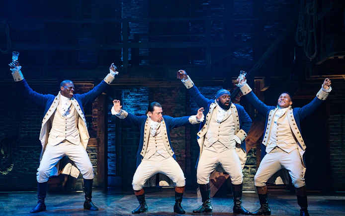 Performers in colonial costumes on stage during a scene from Hamilton musical.