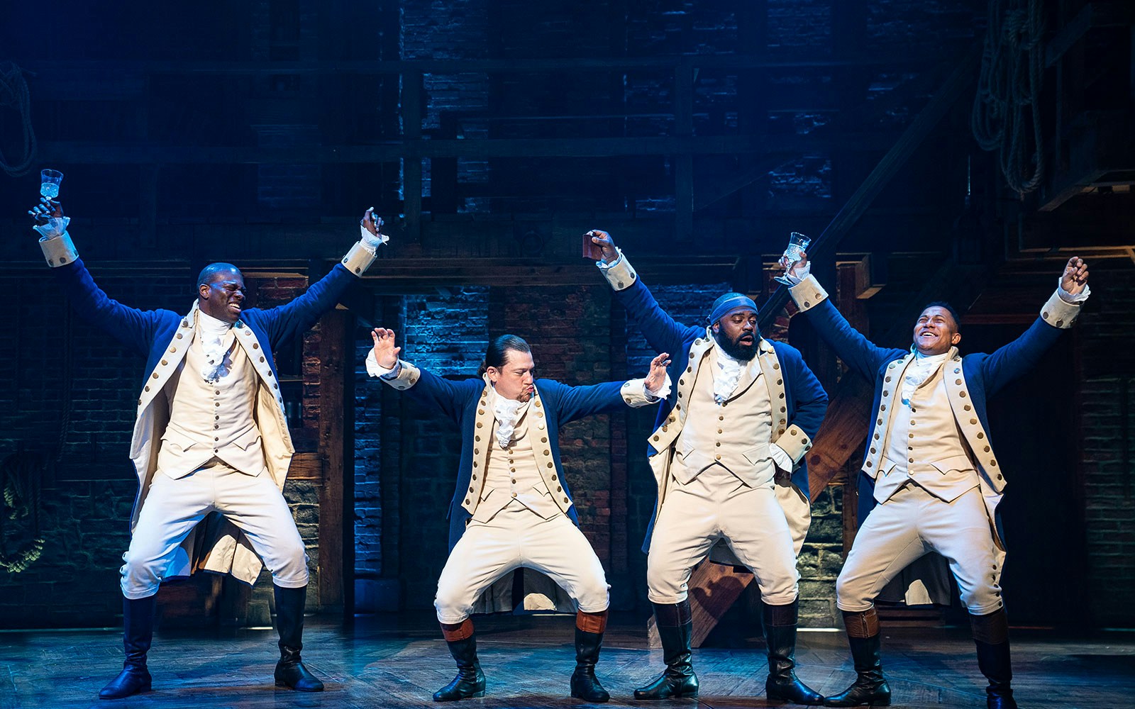 Performers in colonial costumes on stage during a scene from Hamilton musical.