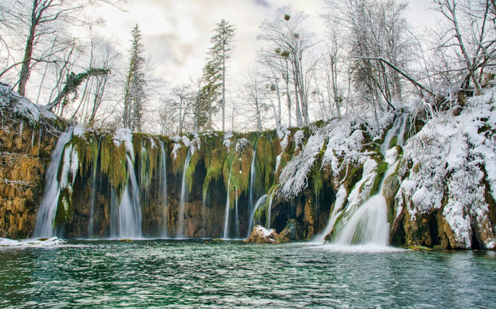 Waterfalls at Plitvice Lakes surrounded by snow-covered trees in winter.