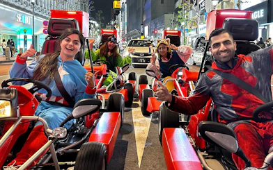 People in costumes driving go-karts on a street in Akihabara at night.