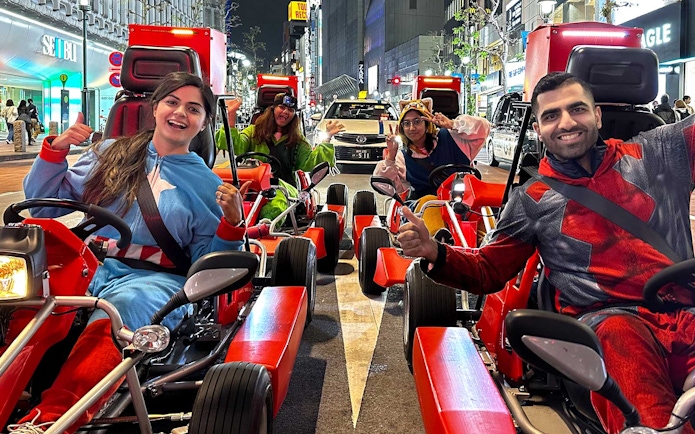 People in costumes driving go-karts on a street in Akihabara at night.