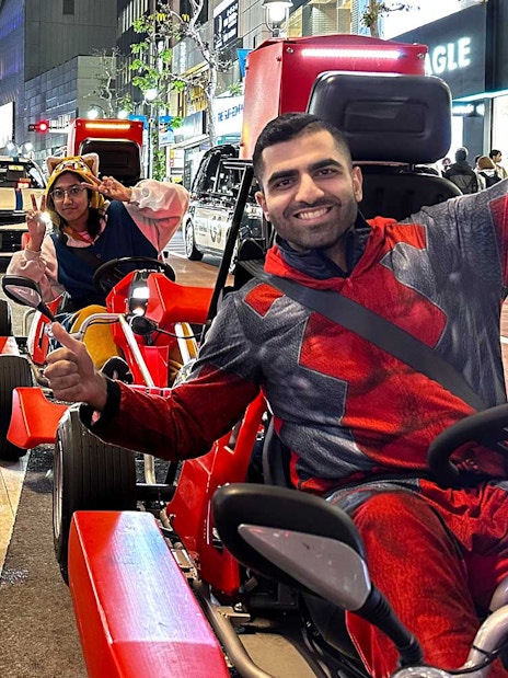 People in costumes driving go-karts on a street in Akihabara at night.