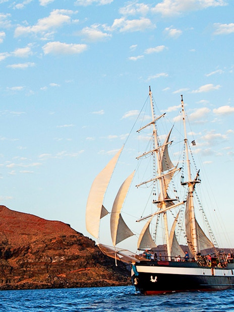 Sailing ship near volcanic island at sunset during dinner cruise.