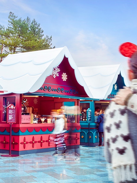 Disneyland Paris Christmas market stalls with visitors in festive attire, 2025.