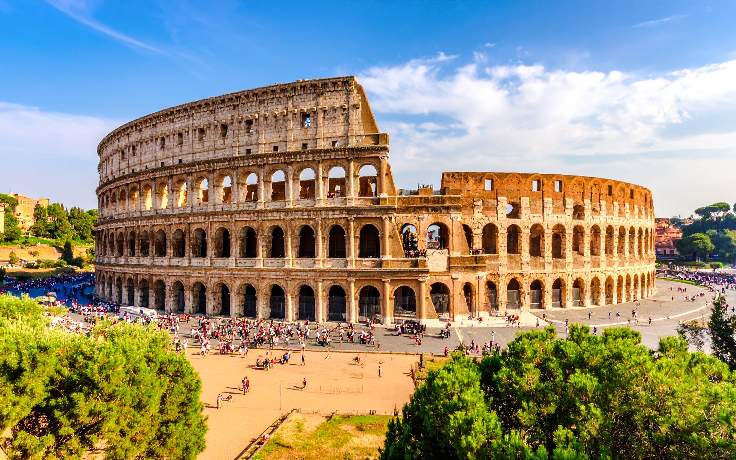 Wide view of the Colosseum in Rome with tourists exploring the ancient amphitheater.
