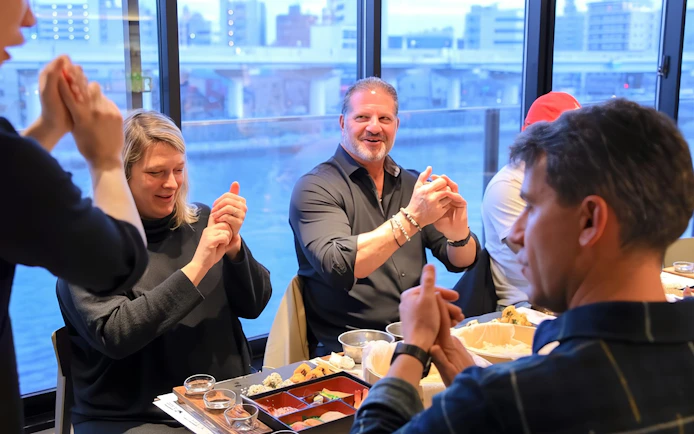 Friends learning sushi making in Asakusa, Tokyo, with cityscape view.