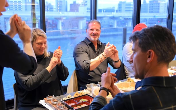 Friends learning sushi making in Asakusa, Tokyo, with cityscape view.