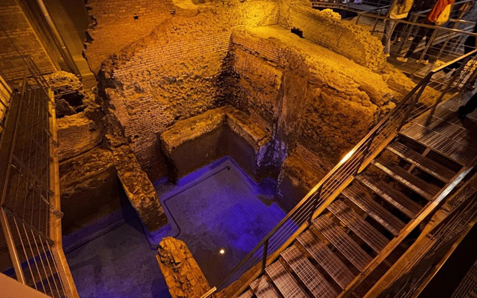 Subterranean aqueduct ruins beneath Piazza Navona, Rome, with ancient brick walls and metal walkways.
