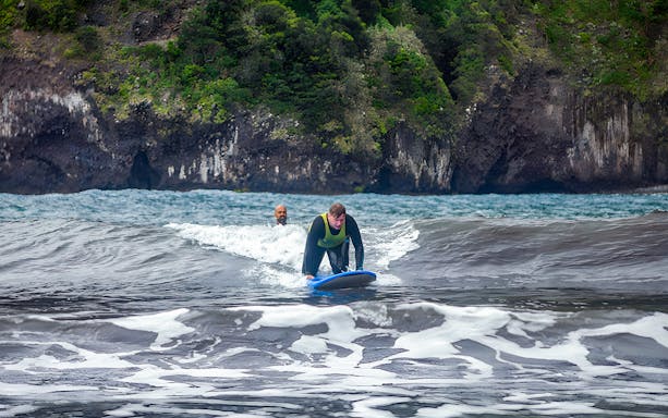 Surfer riding a wave near rocky cliffs in Madeira, Portugal.