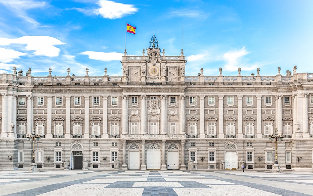 Royal Palace of Madrid facade with Spanish flag under blue sky.