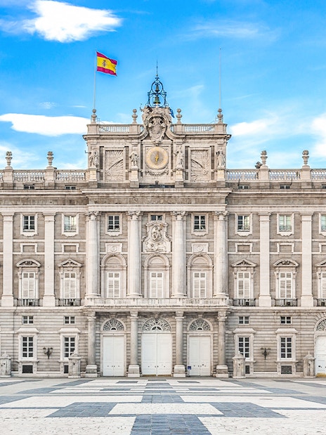 Royal Palace of Madrid facade with Spanish flag under blue sky.