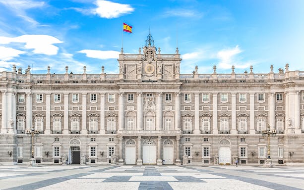 Royal Palace of Madrid facade with Spanish flag under blue sky.