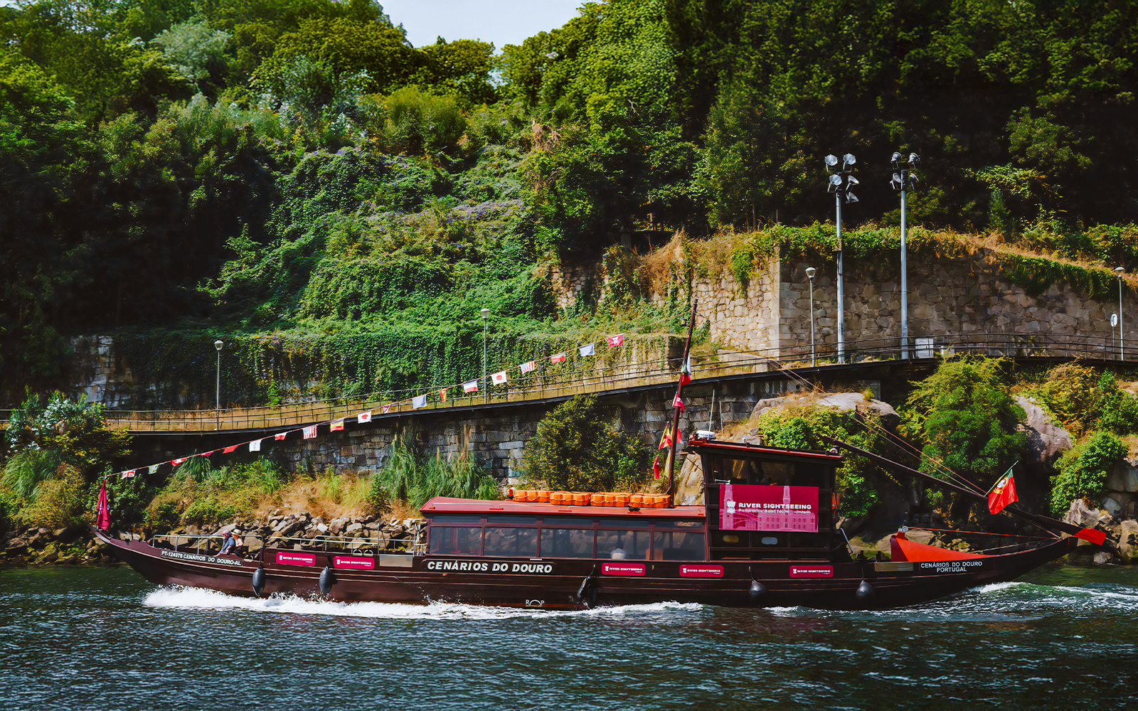 Tourist enjoying a boat ride on the Douro River in Porto, Portugal, with lush greenery in the background.