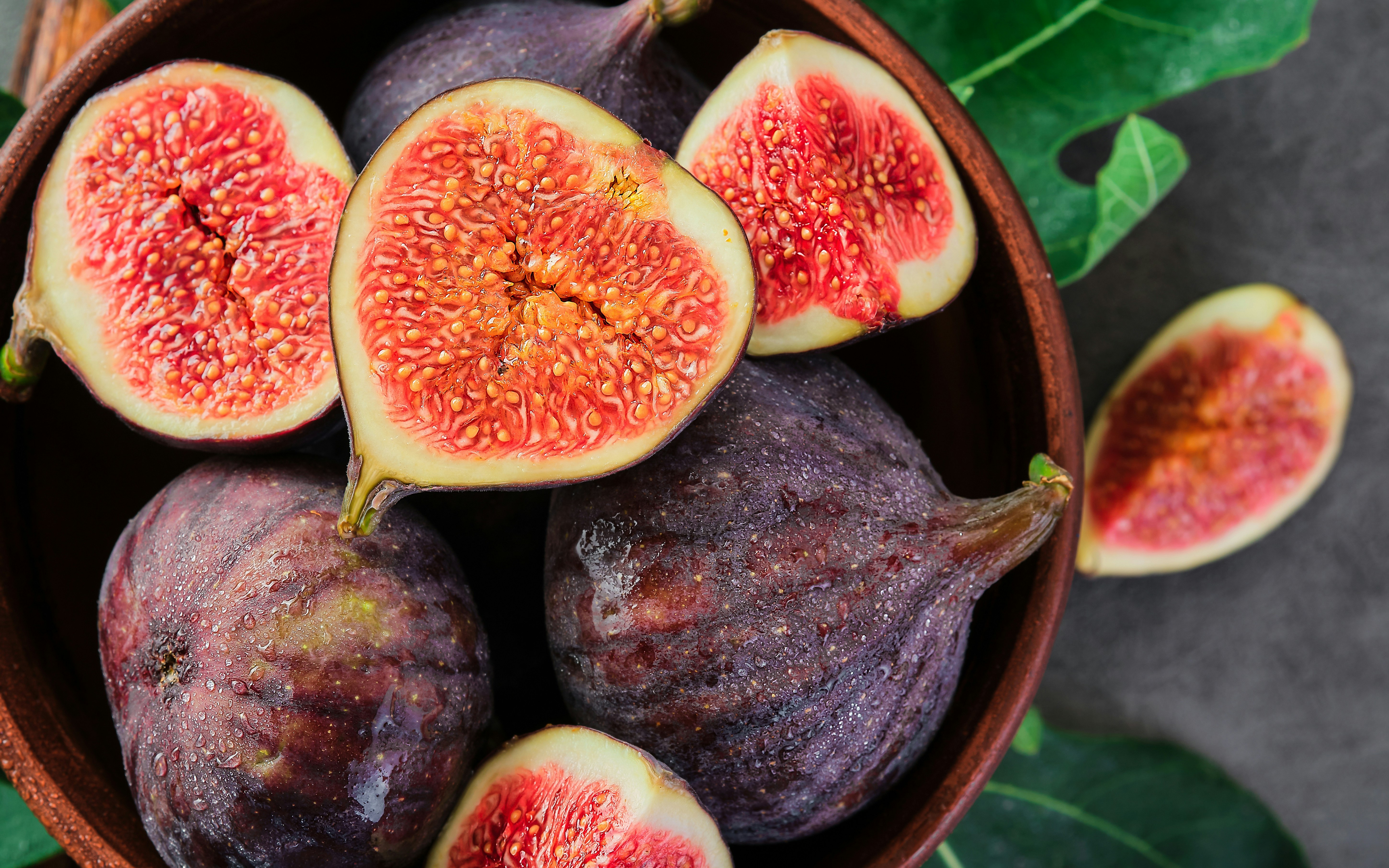 Purple figs in a bowl, some halved to reveal red interiors.