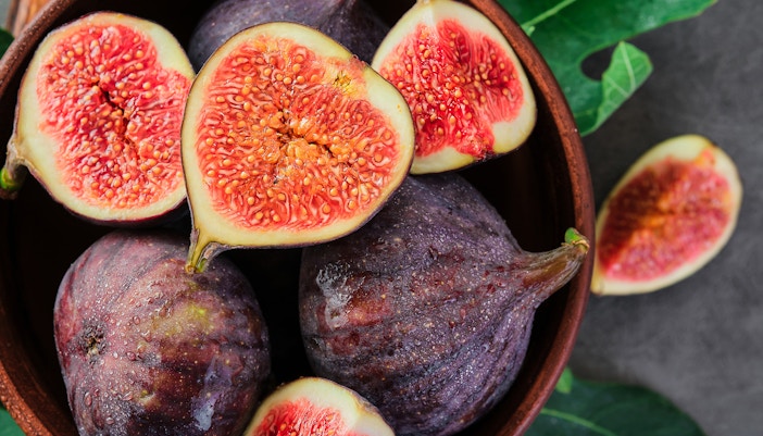 Purple figs in a bowl, some halved to reveal red interiors.