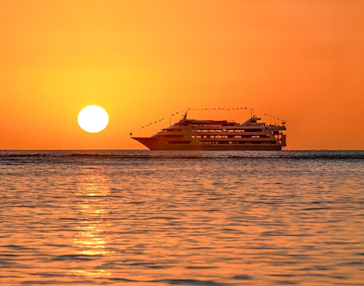 Star of Honolulu cruise ship at sunset with amber sky and ocean.