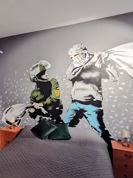 Banksy mural of a pillow fight between a soldier and a masked figure on a bedroom wall.