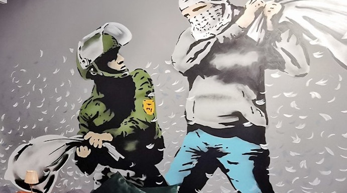 Banksy mural of a pillow fight between a soldier and a masked figure on a bedroom wall.