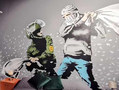 Banksy mural of a pillow fight between a soldier and a masked figure on a bedroom wall.