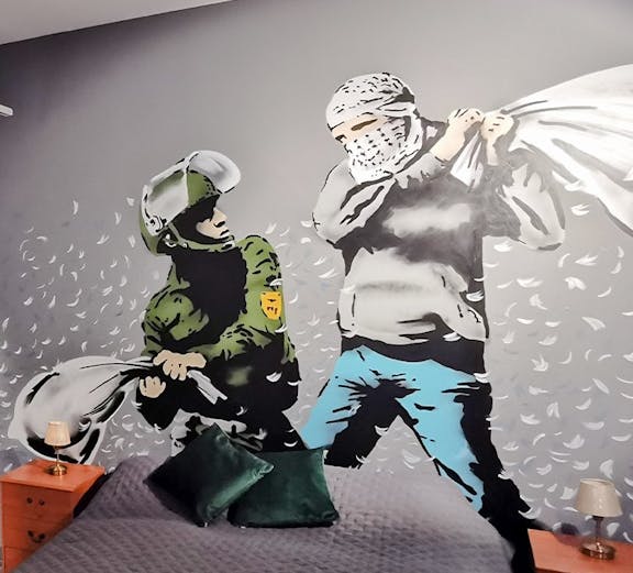Banksy mural of a pillow fight between a soldier and a masked figure on a bedroom wall.