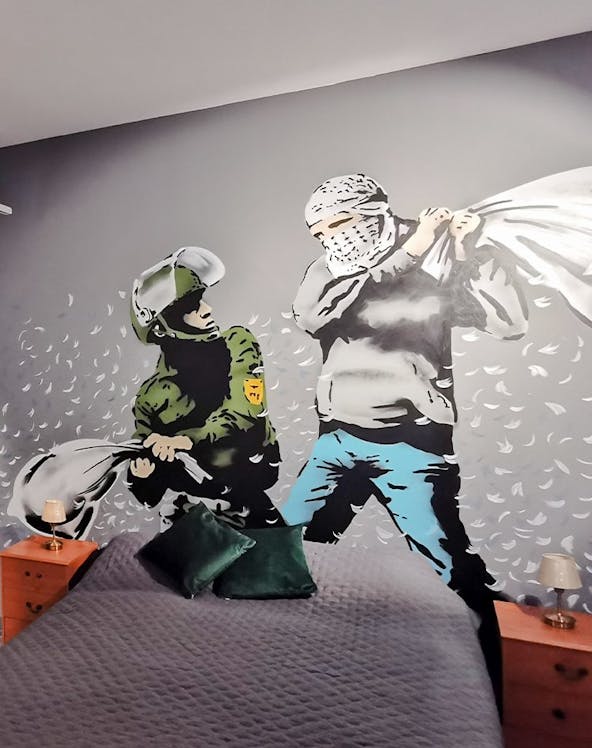 Banksy mural of a pillow fight between a soldier and a masked figure on a bedroom wall.