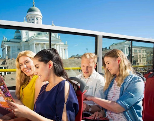 Visitantes no passeio de ônibus Hop-on Hop-off de Helsinque, com a Catedral de Helsinque ao fundo.