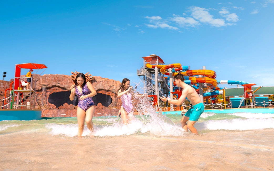 People enjoying the wave pool at Whitewater World with colorful slides in the background.