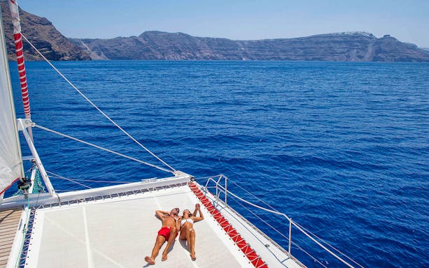 Couple relaxing on catamaran deck during Santorini cruise with caldera view.