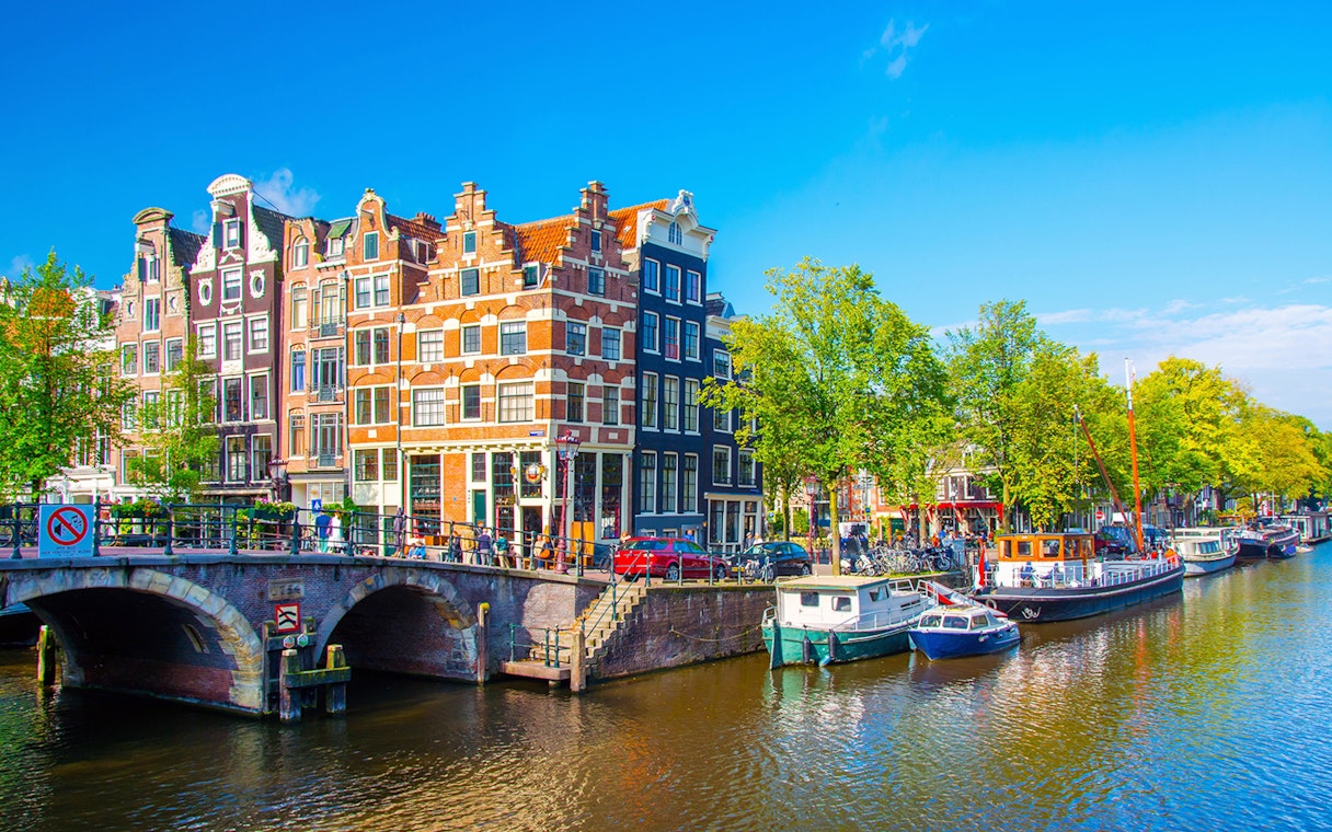 Amsterdam canal with historic buildings and boats, part of a self-guided walking tour.