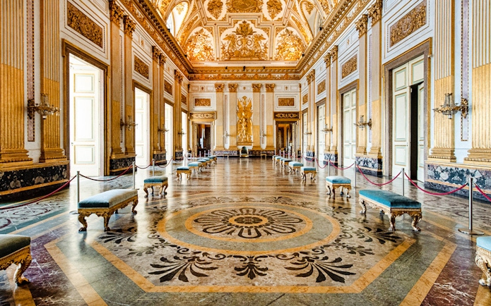 Ornate hall with gilded ceiling and marble floor inside Royal Palace of Caserta.
