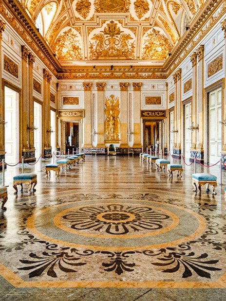 Ornate hall with gilded ceiling and marble floor inside Royal Palace of Caserta.