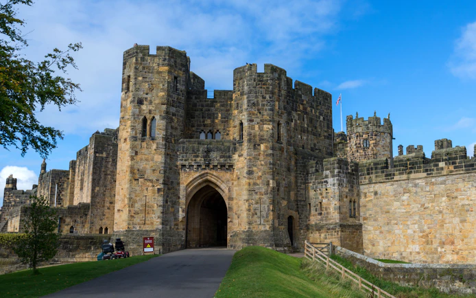 Alnwick Castle entrance with stone archway and towers under a blue sky.