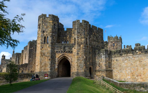 Alnwick Castle entrance with stone archway and towers under a blue sky.