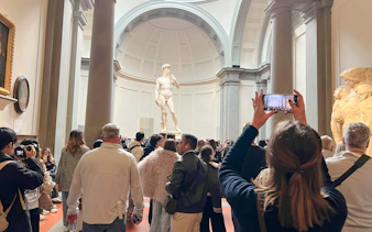 Visitors viewing Michelangelo's David at Academia Gallery, Florence, with audio guides.