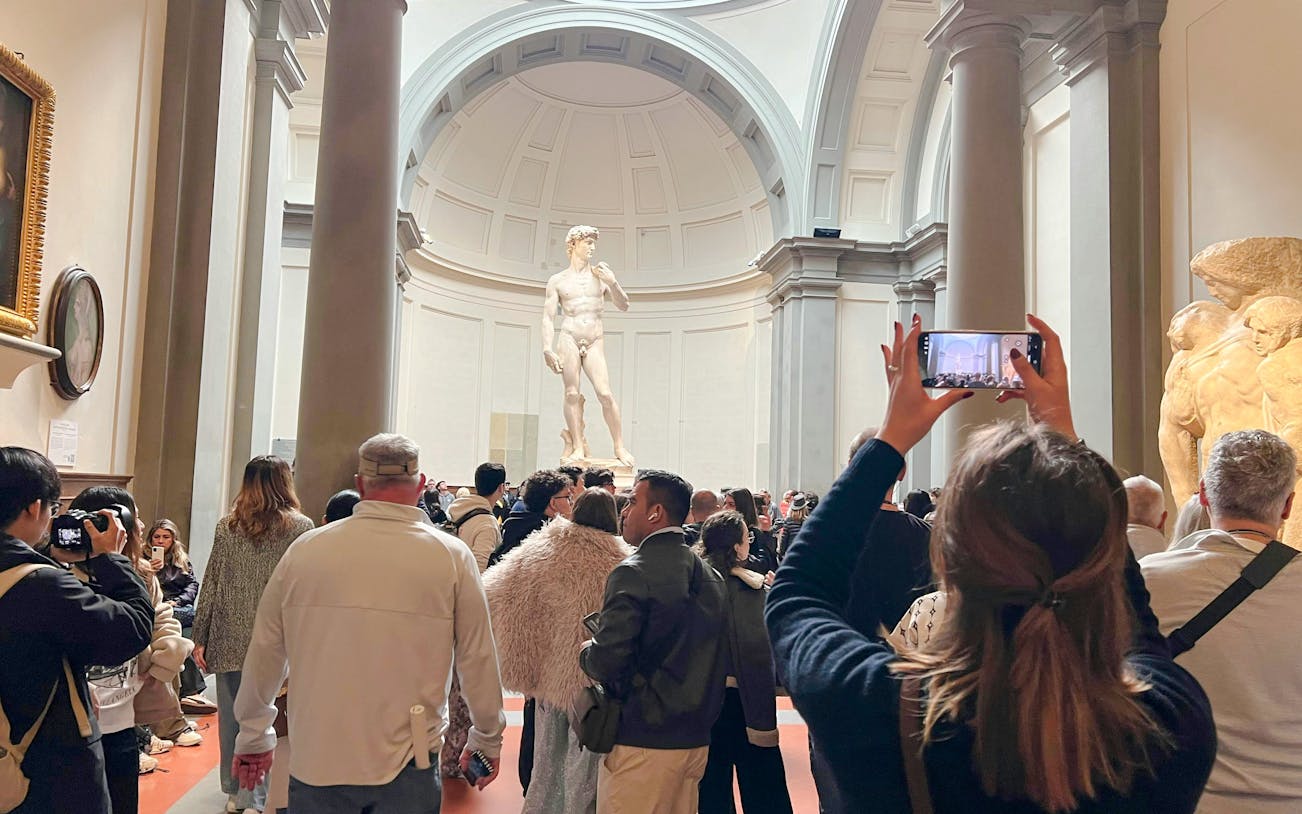 Visitors viewing Michelangelo's David at Academia Gallery, Florence, with audio guides.