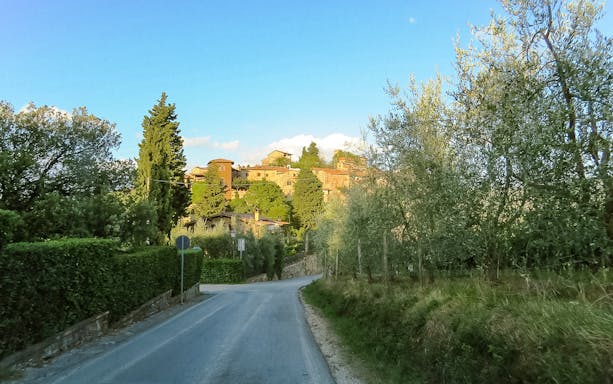 Road through Tuscan countryside with distant village and olive trees.