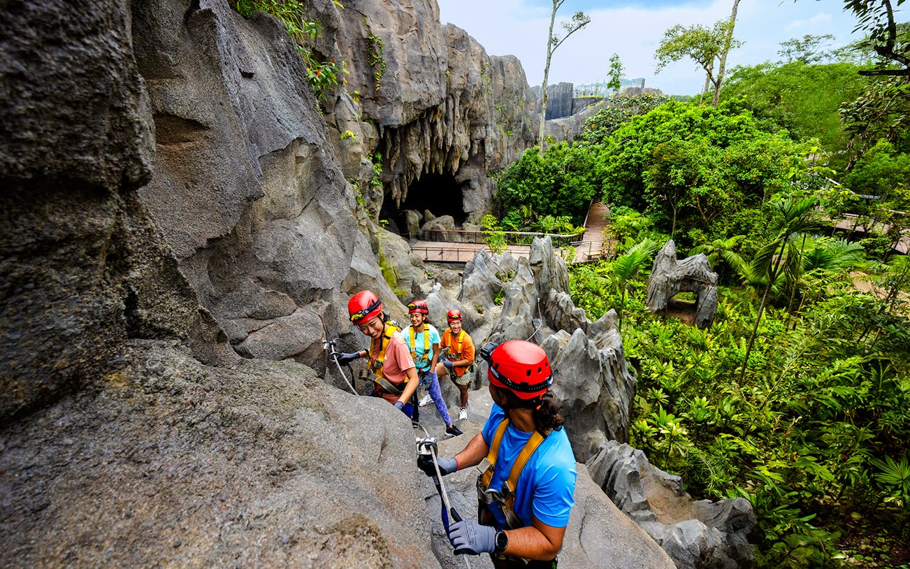 Adventurers climbing rocks in a rainforest cavern in Asia.