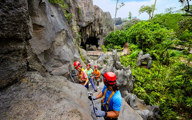 Adventurers climbing rocks in a rainforest cavern in Asia.