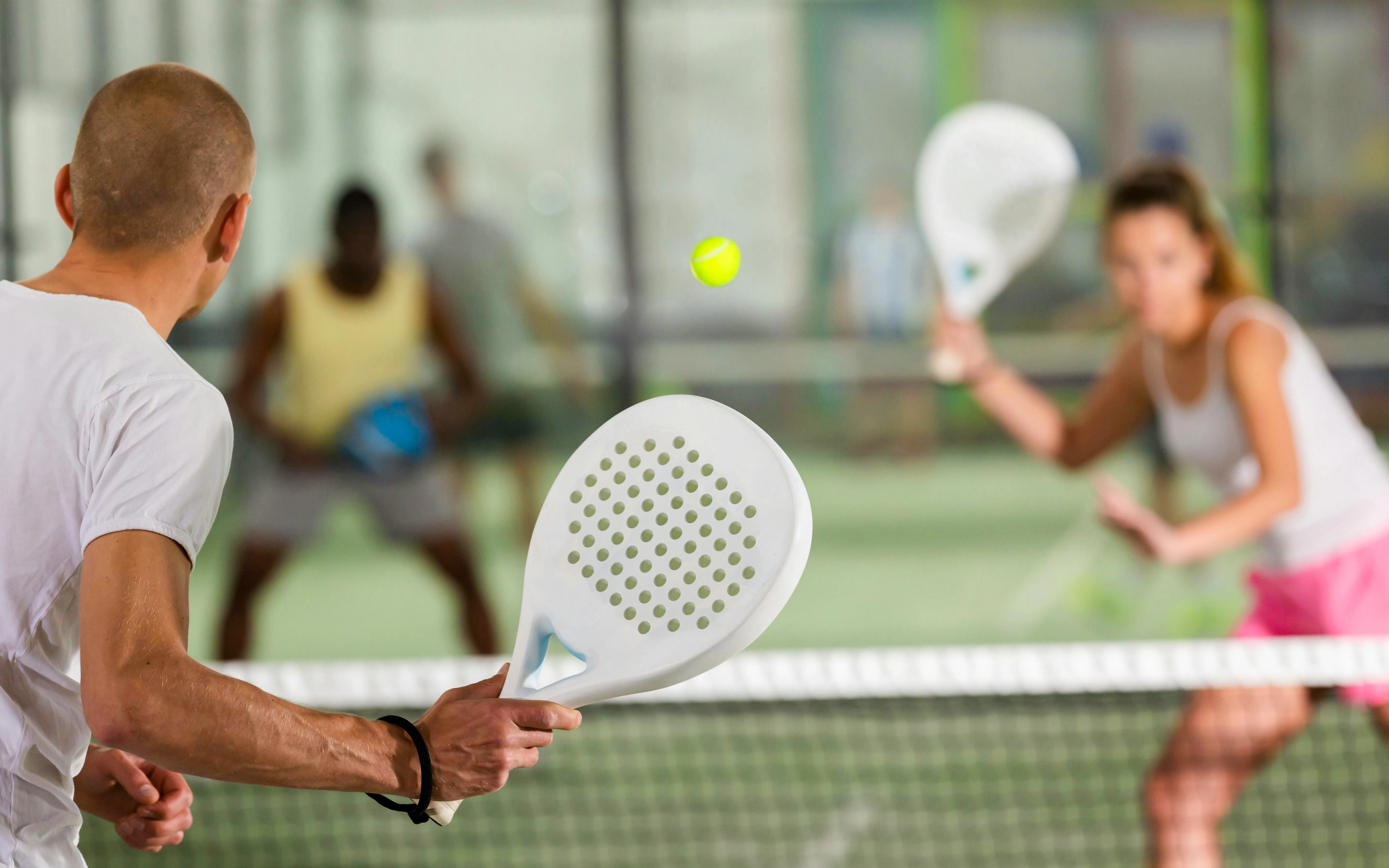 Man playing padel tennis on court, returning a shot with a paddle.